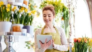 A florist in her shop holding up an iPad to check orders and stock levels.