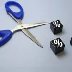 Blue-handled scissors cutting through cubes marked with percentage signs, symbolising 2025 business rate cuts and growth opportunities.