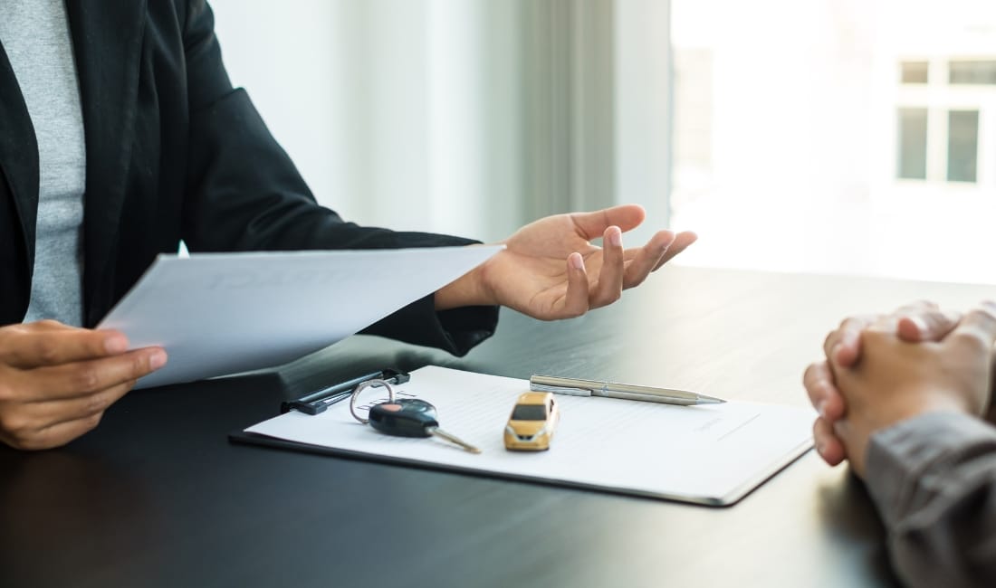 Two people making an asset finance deal with a clipboard and a model car