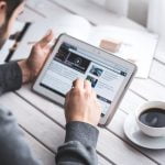 A man in a cafe reading through an article on an Apple iPad