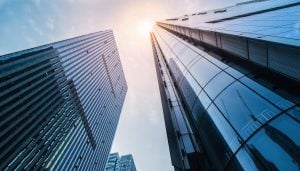 A photo looking up at two skyscrapers with the sun shining through