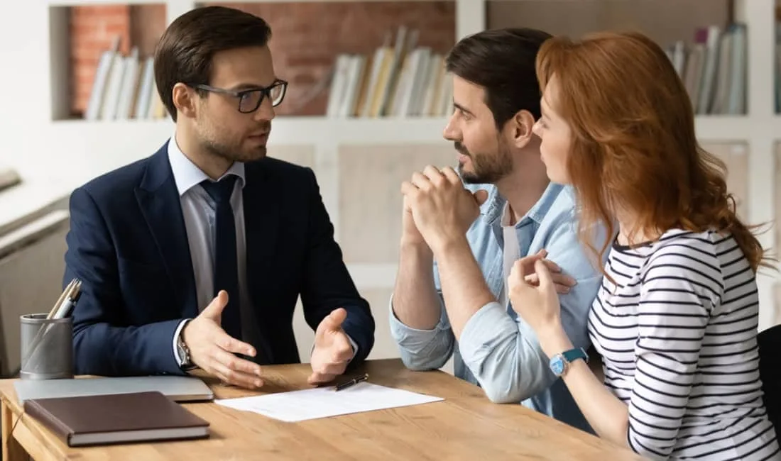 Man in a suit showing dedication to customer retention explaining paperwork to a couple seated at a desk during a financial consultation