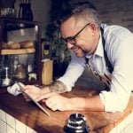 Cafe owner leaning over the counter whilst smiling and pointing to something on his iPad