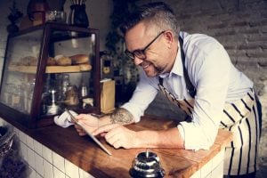 Cafe owner leaning over the counter whilst smiling and pointing to something on his iPad