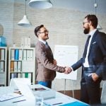 Two professionals smile and shake hands in an office environment