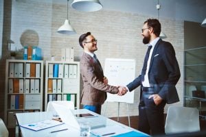 Two professionals smile and shake hands in an office environment