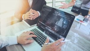 Close up of three professionals in a meeting referring to graphs and pie charts which are displayed on a laptop