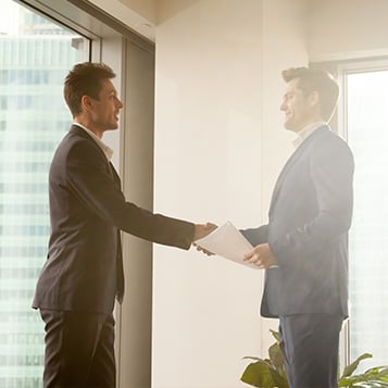 good-meeting Two smartly dressed professionals shaking hands and smiling at one another in an office environment