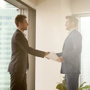 Two smartly dressed professionals shaking hands and smiling at one another in an office environment