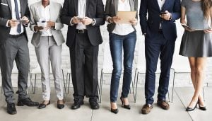 6 professionals stood next to one another whilst holding various items such as documents, phones and iPads