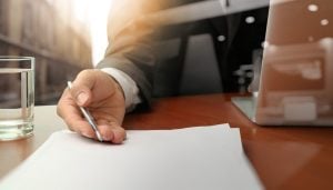 Close up of a businessman holding a pen against paper next to a laptop