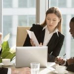 Three professionals in a business meeting discussing and referring to company financials