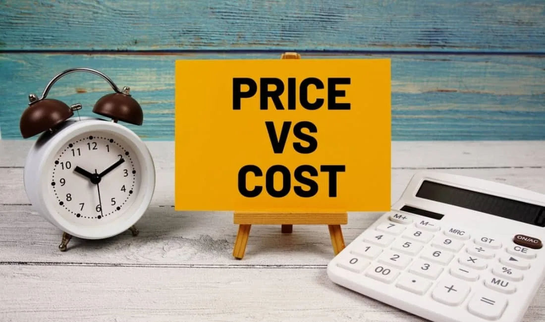 Sign reading "PRICE VS COST" sales tactic placed between a clock and a calculator on a wooden surface