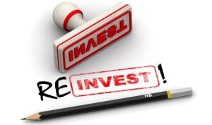Rubber stamp marked “INVEST” with a pencil spelling out the word reinvest, symbolising reinvestment with business finance.