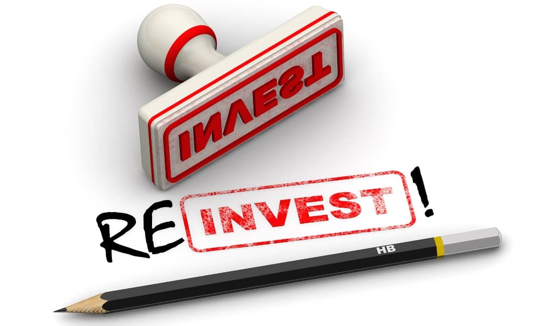Rubber stamp marked “INVEST” with a pencil spelling out the word reinvest, symbolising reinvestment with business finance.