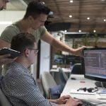 Software developers gathered around a computer screen reading code