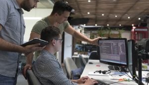 Software developers gathered around a computer screen reading code