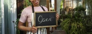 A business owner holding up an 'open' sign in front of her startup cafe