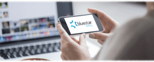 Someone holding up an iPhone with the Bluestar logo displayed on the screen