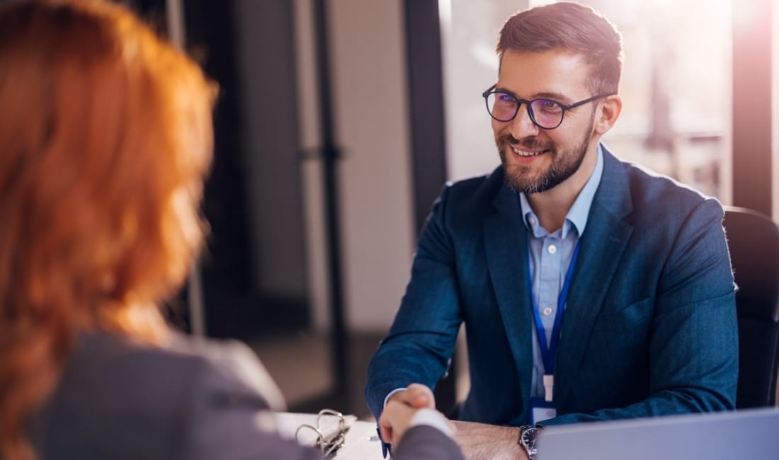 Business professional smiling and shaking hands with a woman in an office setting, suggesting a successful finance meeting